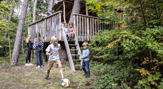 foto cover jaarverslag 2022: kinderen die rond en in de boomhut spelen